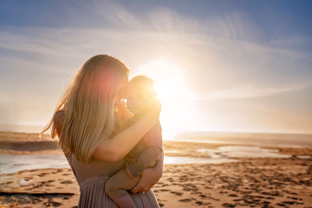 Family Photography, a mother holds baby close before a beach sunset