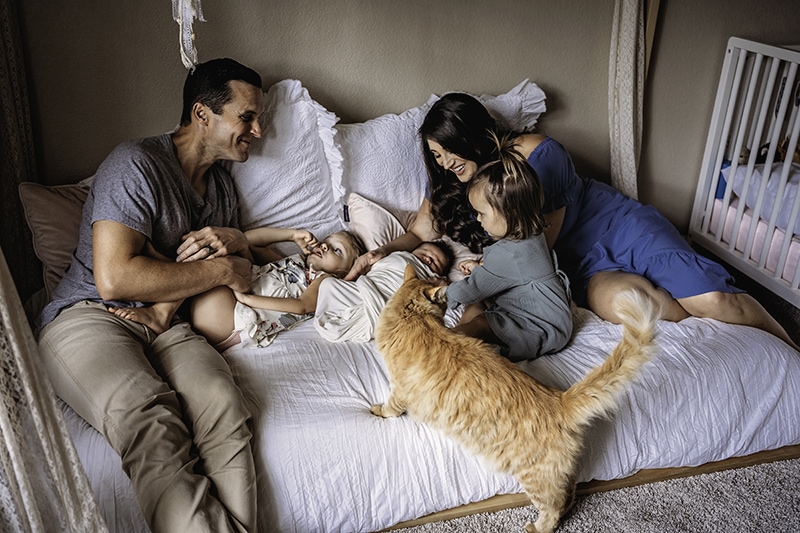 Family Photography, Mom, dad, and older sister tend to two babies, the cat is on the bed with them